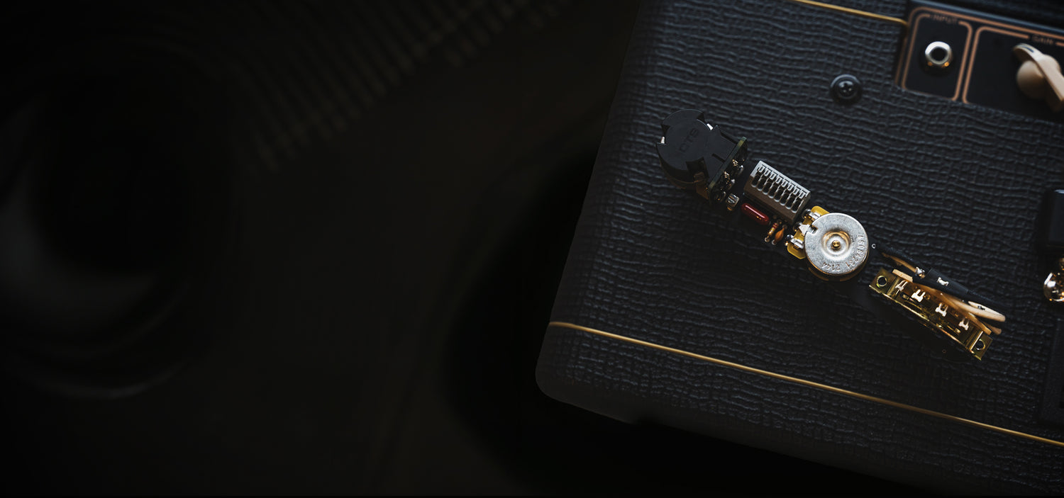 An obsidianwire solderless wiring harness set on top of a black Vox AC10 guitar amp. The background is black to contrast the wiring harness