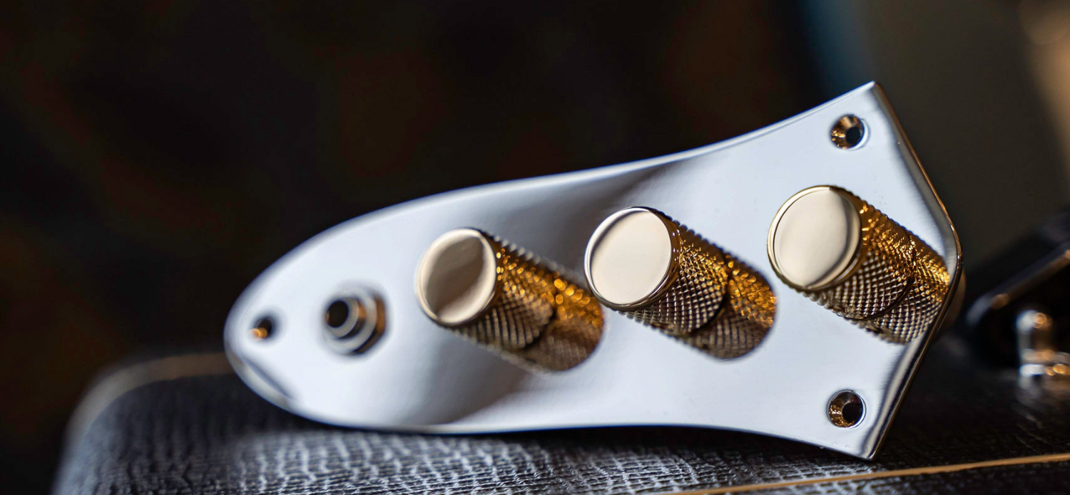 Custom loaded control plate for jazz bass with chrome plate and knurled gold knobs, rested on an amplifier